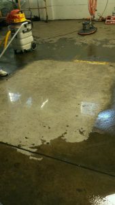 a concrete floor in the process of being polished, showing the old, rough condition of the floor and a large patch that has been shined and is looking great.